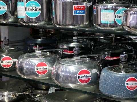 Hawkins and Prestige pressure cookers lined up on a shelf.