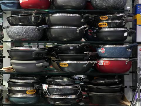 Stacked non-stick kadhai and frying pans on a shop shelf.