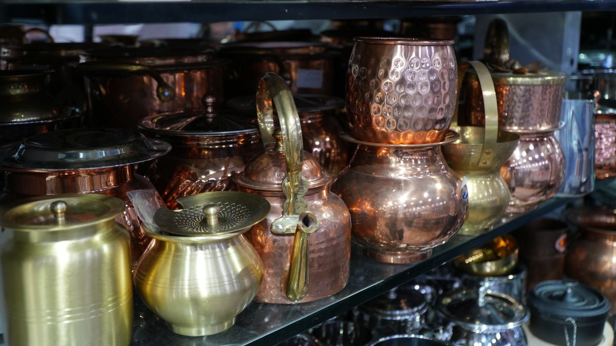 Hammered copper jugs, a copper kettle and polished brass lotas on a shelf at Mahindra Departmental Store, Greater Kailash.