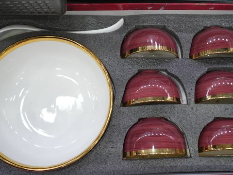 A boxed set of six gold-rimmed bowls and a serving bowl in a presentation case.