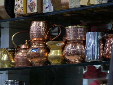 Hammered copper and brass jugs and mugs arranged on a shelf.