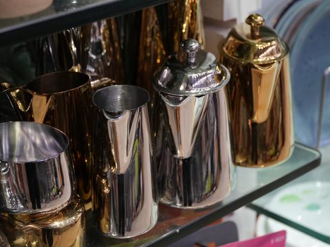 Gold and silver toned jugs and a kettle on a glass shelf.
