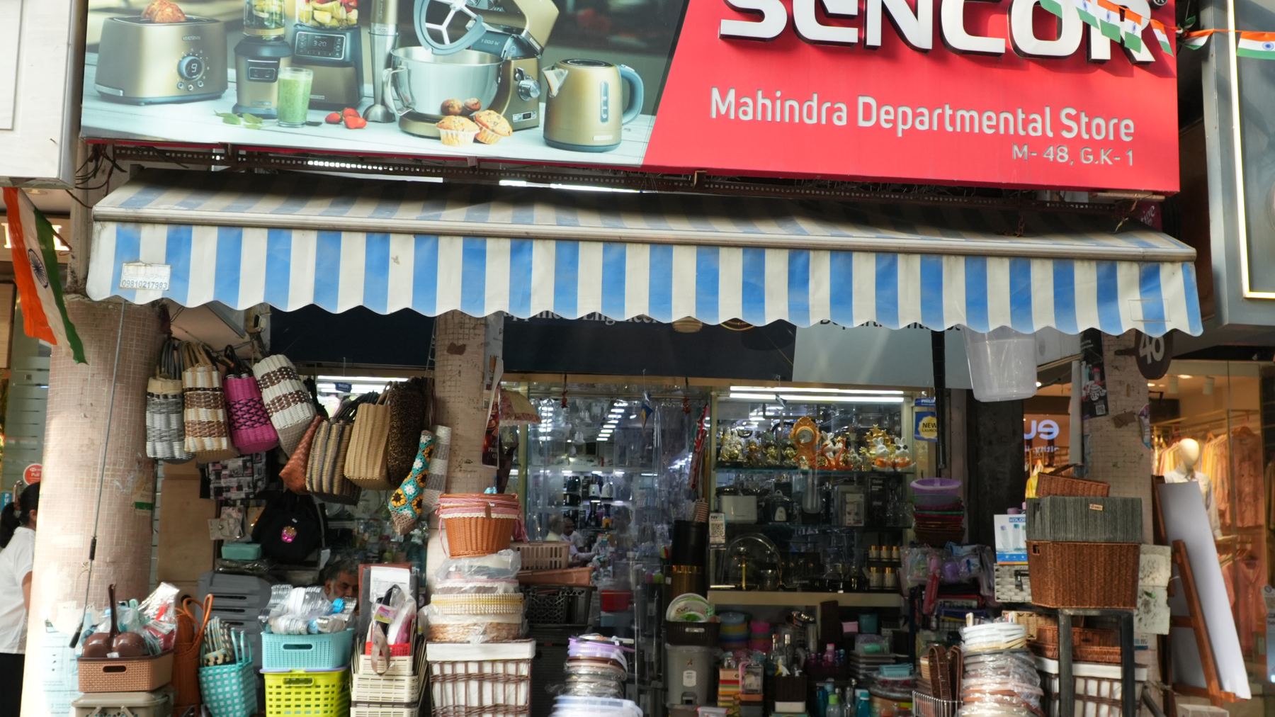 The shopfront of Mahindra Departmental Store at M-48, M Block Market, Greater Kailash-1, under its blue and white striped awning.